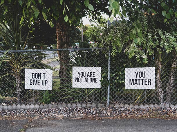 Three printed signs by the pavement reading don't give up, you are not alone, and you matter.