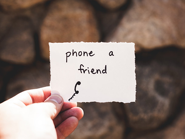 A hand holds a small piece of paper with writing on it. The writing says 'phone a friend' and there's a small drawing of a phone handset.