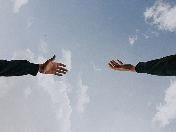 Two hands reach out to each other against a cloudy blue sky.