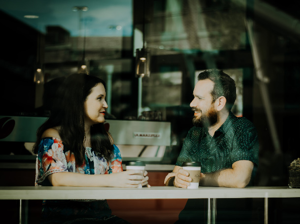 A man and a woman talk while sat at the bar in a coffee shop window. Suicide prevention and talk about suicide thoughts can happen anywhere including public spaces